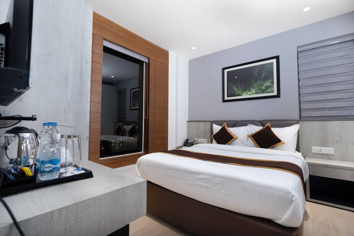 Een moderne hotelkamer met een bed, een televisie, een koffiezetapparaat en een waterfles op een dienblad.