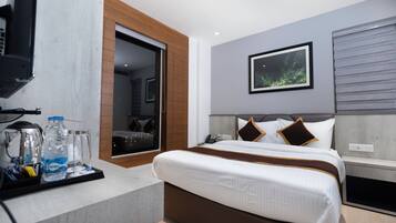 A modern hotel room with a bed, a television, a coffee maker, and a water bottle on a tray.