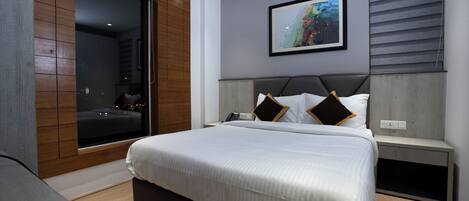Une chambre moderne avec un grand lit, une table de chevet, une commode, une fenêtre avec des stores et un tableau encadré au mur.