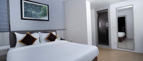 Una habitación de hotel moderna con una cama grande, una obra de arte enmarcada en la pared, un vestidor amplio y un baño visible a través de una puerta de cristal.