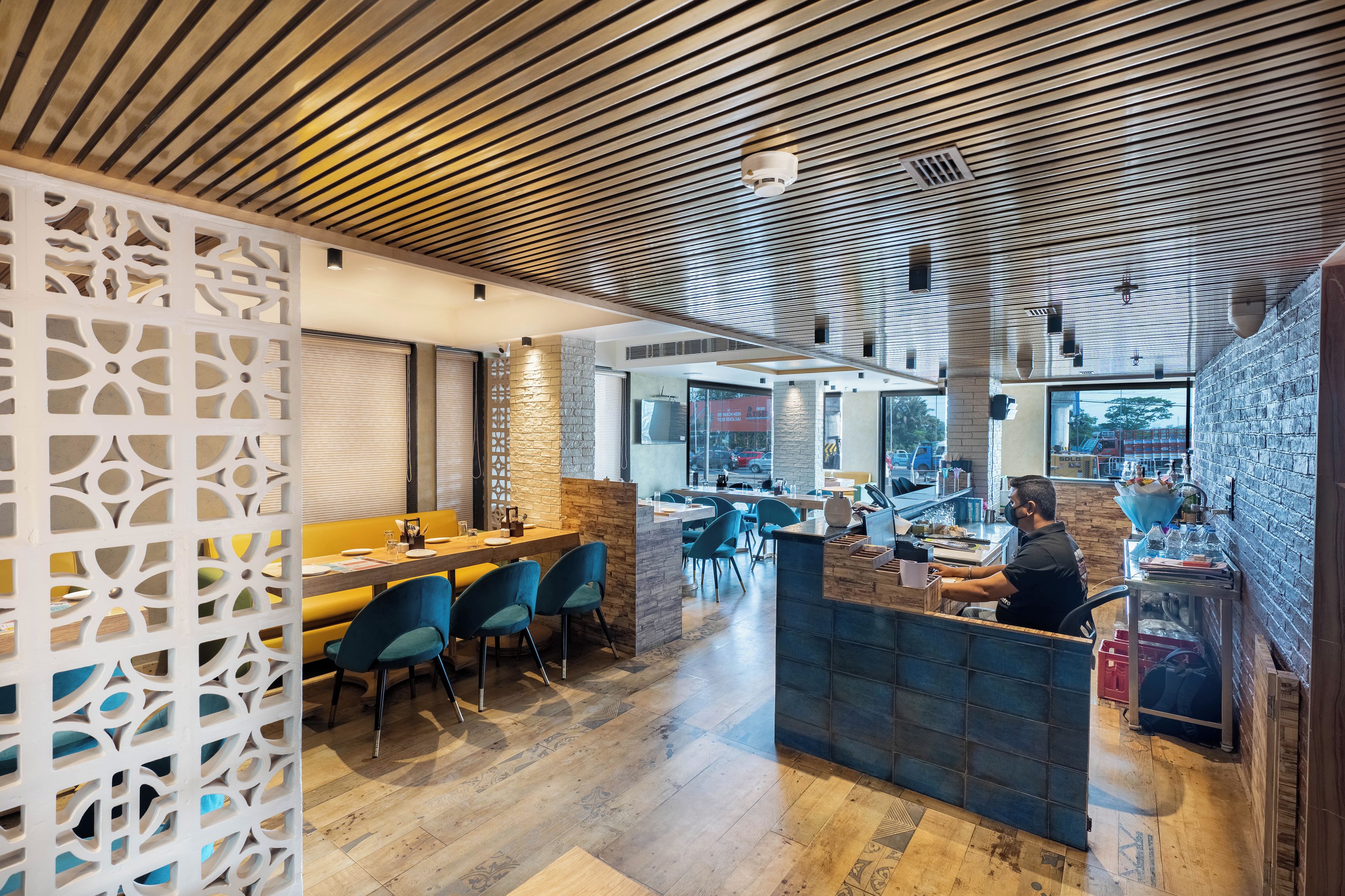 A restaurant interior with wooden ceiling, blue chairs, and a counter.