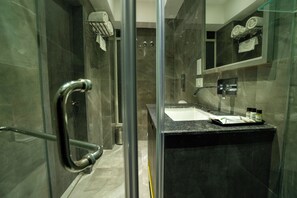 Een moderne badkamer met een douchecabine van glas, een wastafel met donker aanrecht en een spiegel boven de wastafel.
