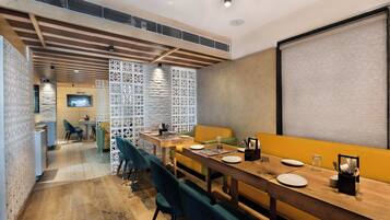 A modern dining area with a long wooden table, multiple chairs, and a television screen.