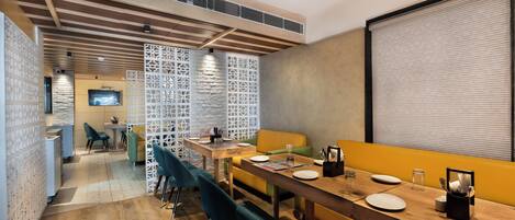 A modern dining area with a long wooden table, multiple chairs, and a television screen.