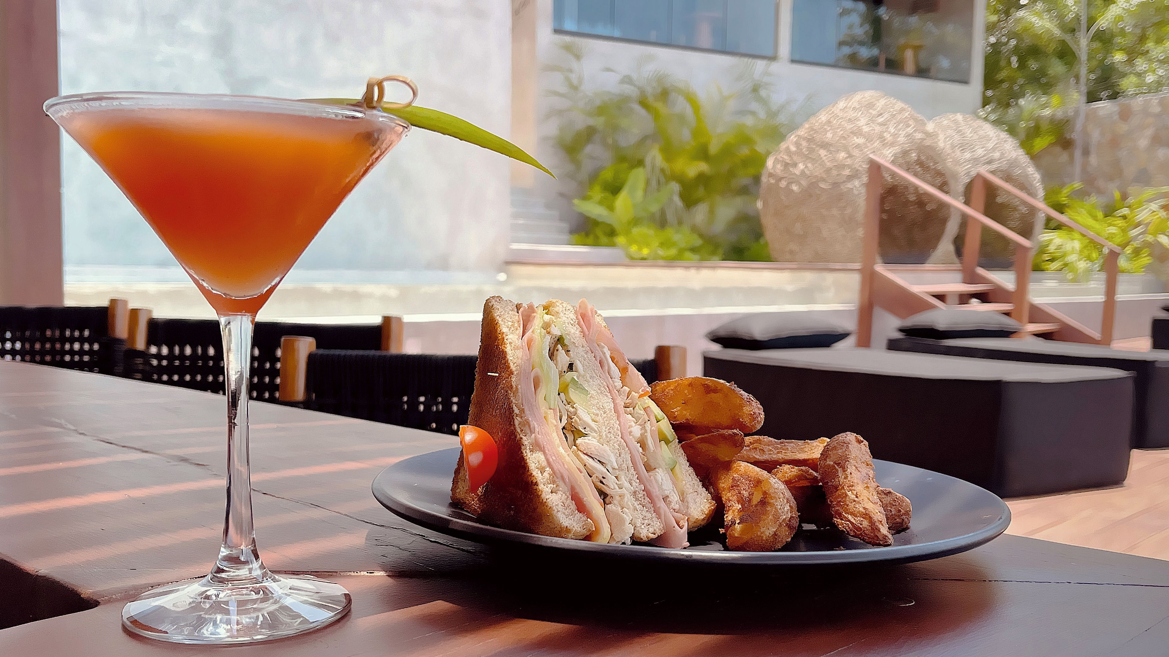 Um copo de martini com um enfeite sobre uma mesa com um prato de comida e aperitivos fritos.
