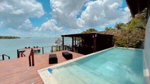 A wooden deck with a pool, a covered seating area, and a view of the sea.