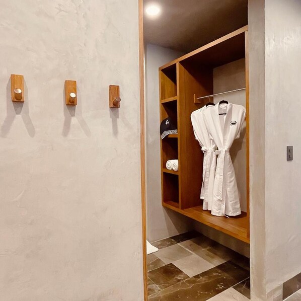 A hotel bathroom with a wooden vanity, a towel rack, and a robe hanging on a rack.