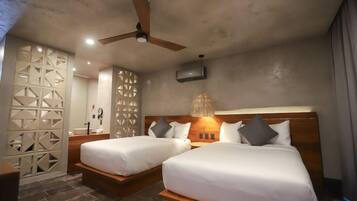 Habitación de hotel con dos camas, ventilador de techo, televisor montado en la pared y una lámpara decorativa.