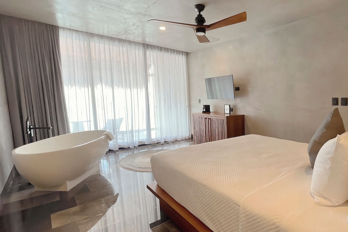 Quarto moderno com cama grande, banheira independente, ventoinha de teto e tapete redondo.