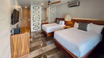 Quarto de hotel com duas camas, televisão, secretária de madeira e ventoinha de teto moderna.