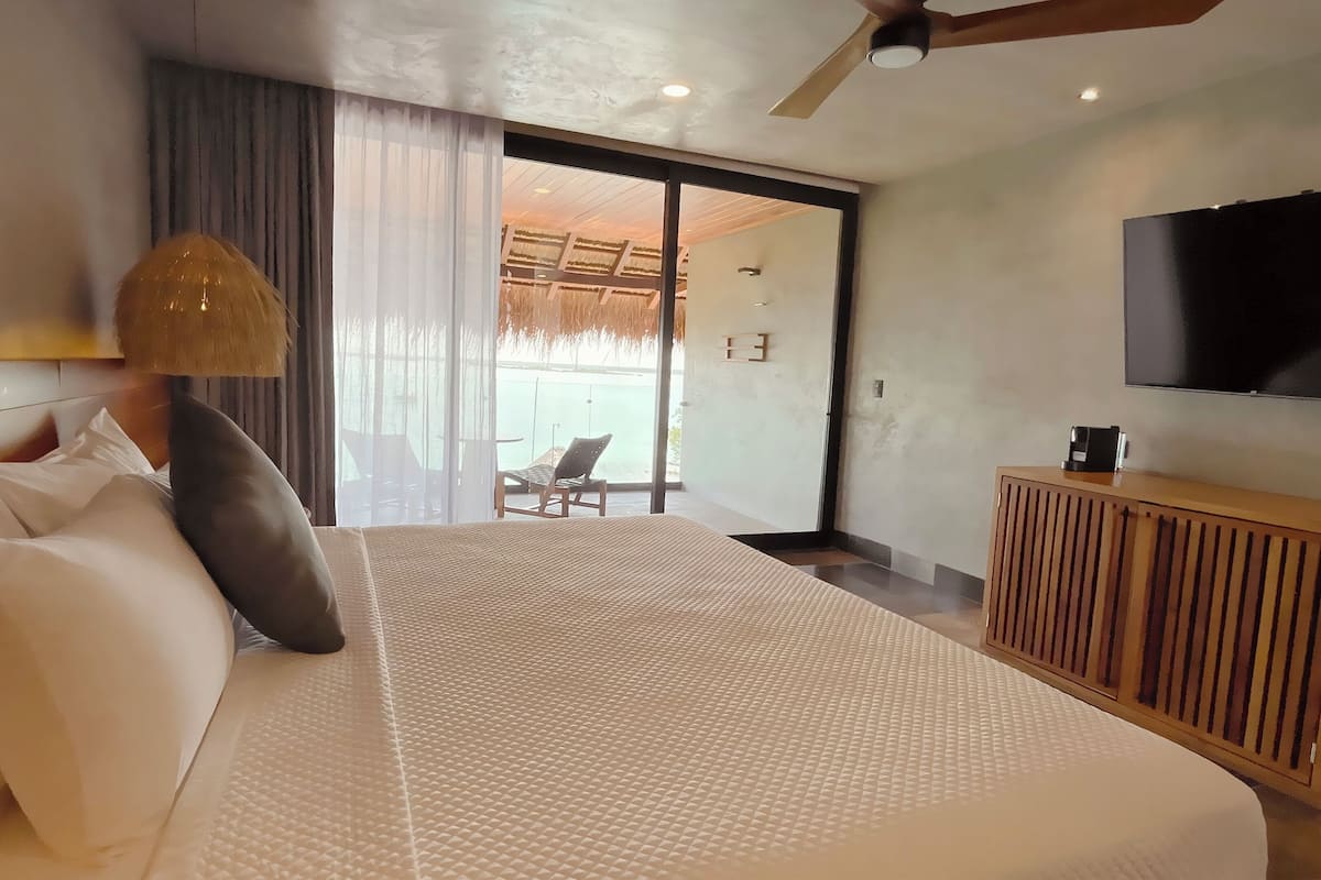 Quarto de hotel moderno com uma cama grande, televisão, armário de madeira e varanda com vista.