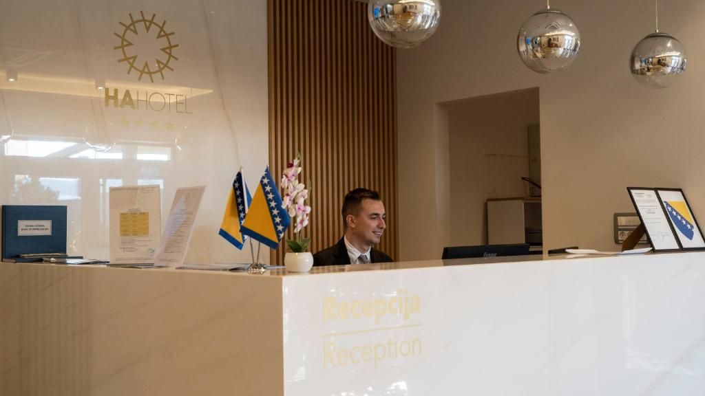 Una mesa de recepción de hotel con cartel de recepción, banderas y un reloj en la pared.