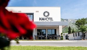 A modern HA HOTEL building with a prominent logo, outdoor seating area, and a view of the surrounding landscape. - Ha Hotel (Mostar)