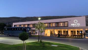 A modern hotel with a flat roof, a dining area with outdoor seating, and a bus parked in front.