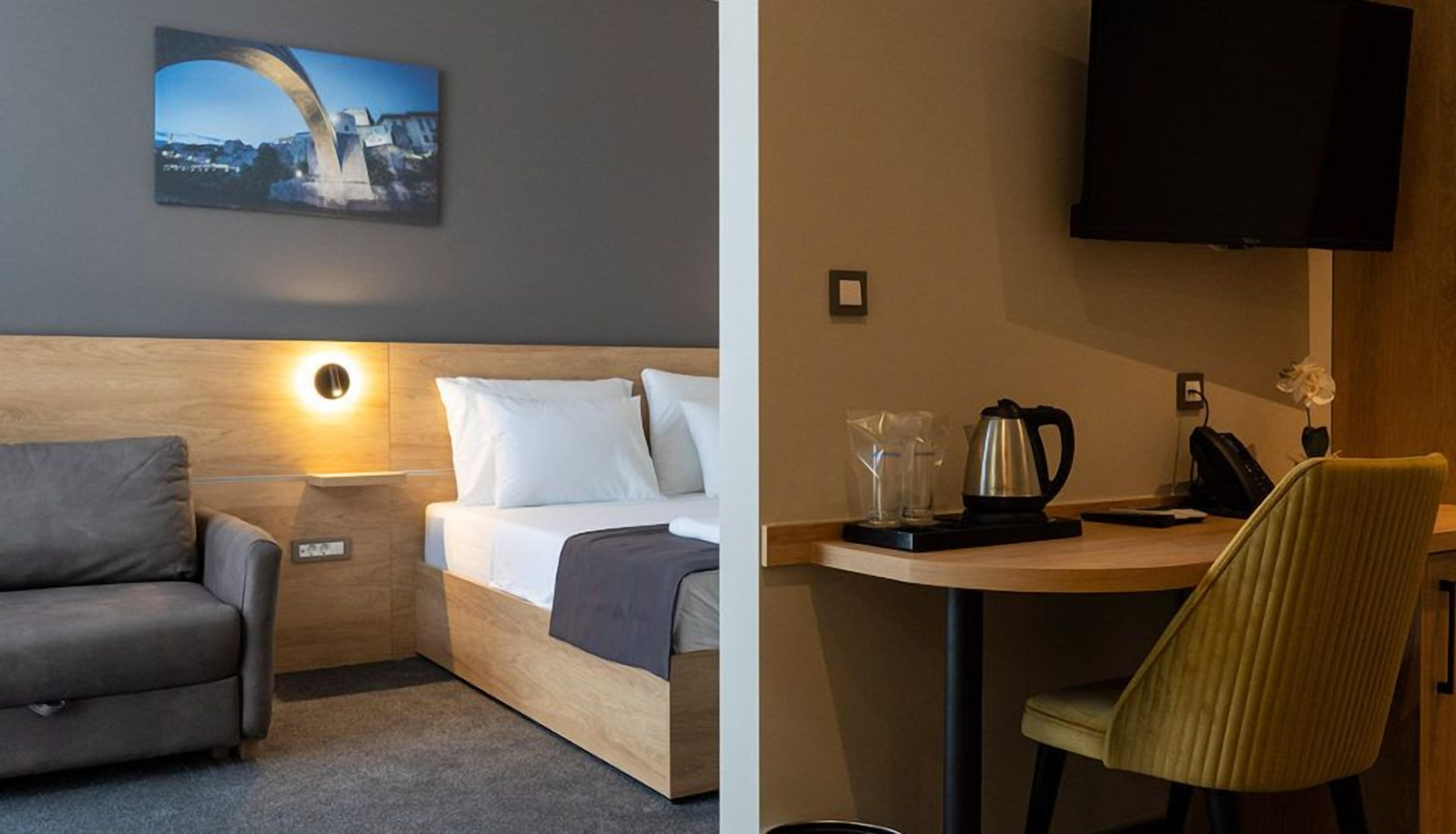 Een hotelkamer met een bed, een slaapbank, een bureau met stoel, een televisie en een schilderij aan de muur.