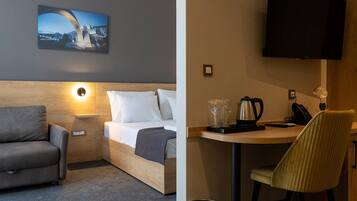 Een hotelkamer met een bed, een slaapbank, een bureau met stoel, een televisie en een schilderij aan de muur.