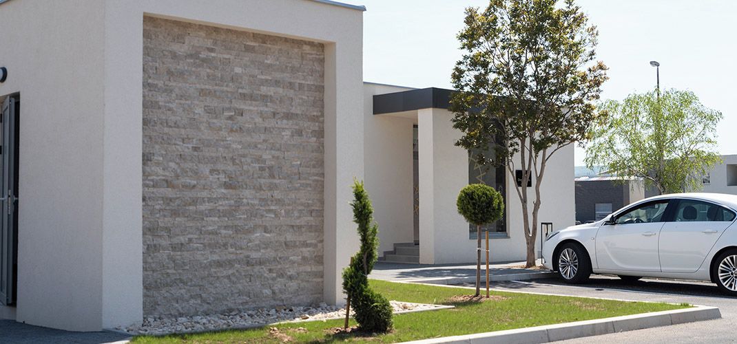 Un bâtiment moderne avec une façade en briques, une voiture blanche garée devant et un petit arbre dans la cour.