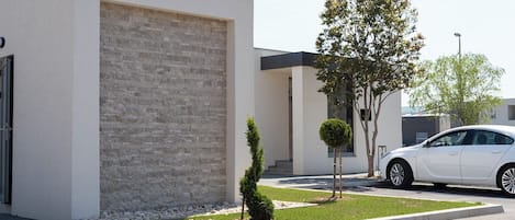 Un bâtiment moderne avec une façade en briques, une voiture blanche garée devant et un petit arbre dans la cour.