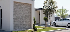Edifici modern amb façana de maó, un cotxe blanc a la part del davant i un petit arbre al jardí.