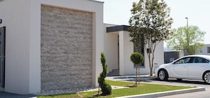Un bâtiment moderne avec une façade en briques, une voiture blanche garée devant et un petit arbre dans la cour.
