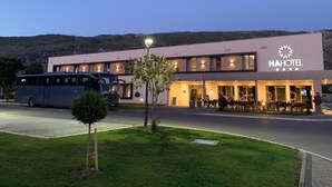 Un hotel moderno con techo plano, zona de comedor con mesas al aire libre y un autobús estacionado frente.