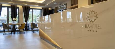 Zona de recepción de un hotel con diseño moderno, una mesa de recepción y un área de estar con sillas y una mesa.