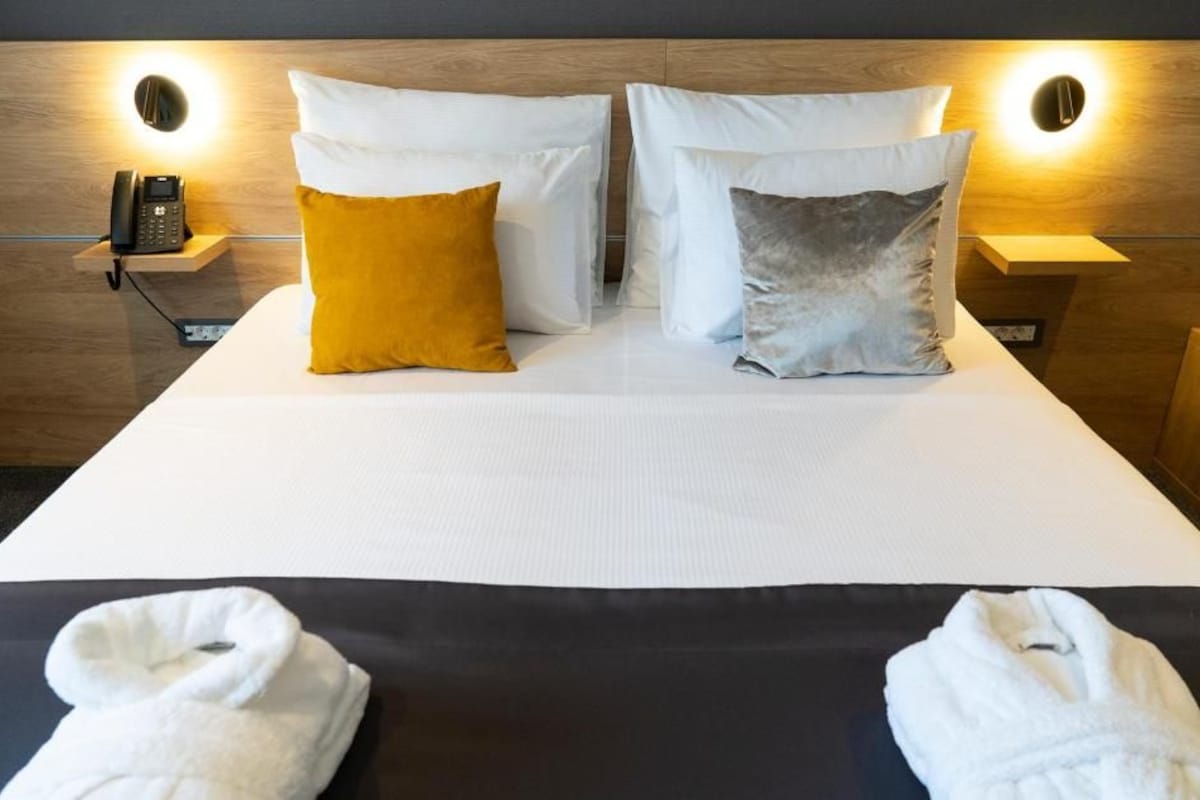 A hotel room with a bed, two bedside lamps, a phone, and two towels.