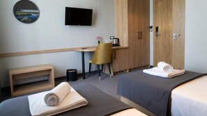 Ein Hotelzimmer mit zwei Betten, einem Schreibtisch mit Stuhl, einem Fernseher und einem Kleiderschrank.