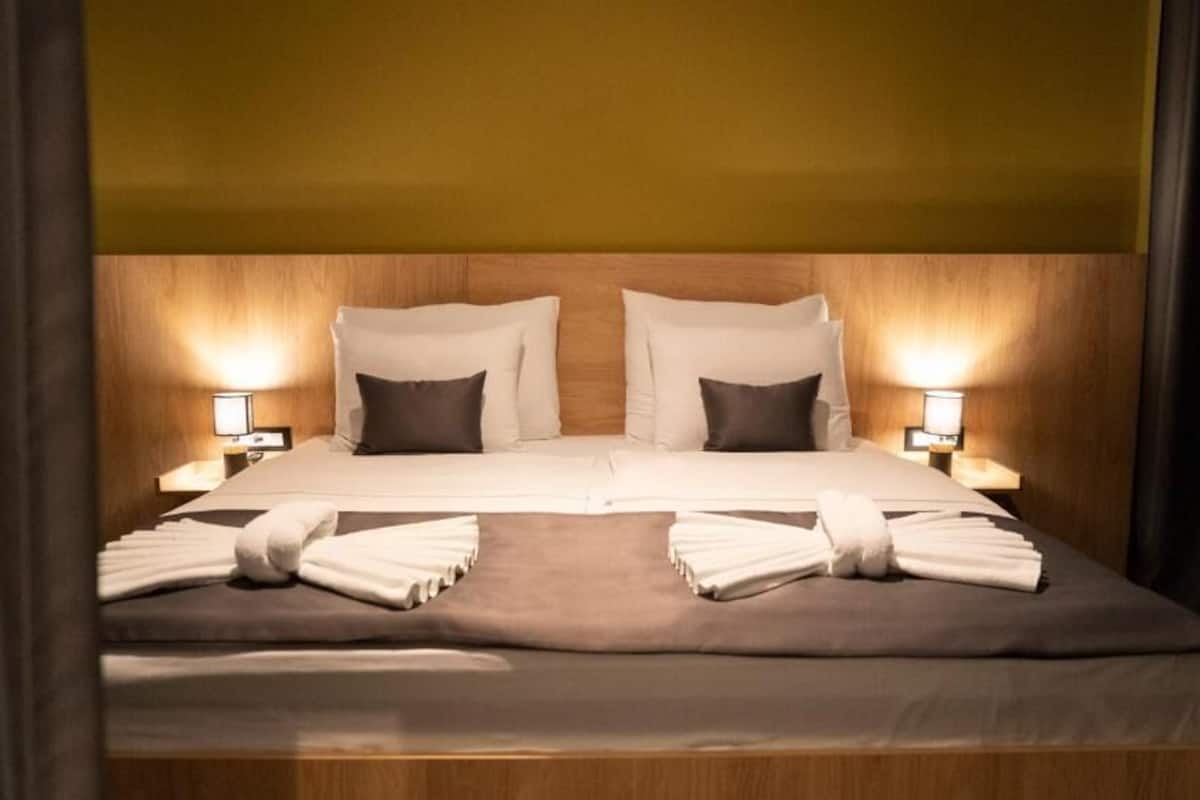 Uma cama de casal com cabeceira de madeira, duas luminárias de cabeceira e toalhas dobradas com cuidado.