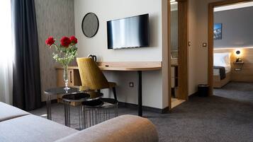 Habitación de hotel con cama, televisor montado en la pared, una pequeña mesa con sillas, un florero con flores y un escritorio de madera.