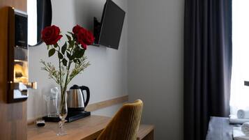 A hotel room with a wooden desk, a vase with red roses, a coffee maker, and a television on the wall.