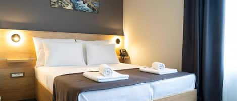 A hotel room with a bed, two bedside tables, a painting on the wall, and a window with curtains.