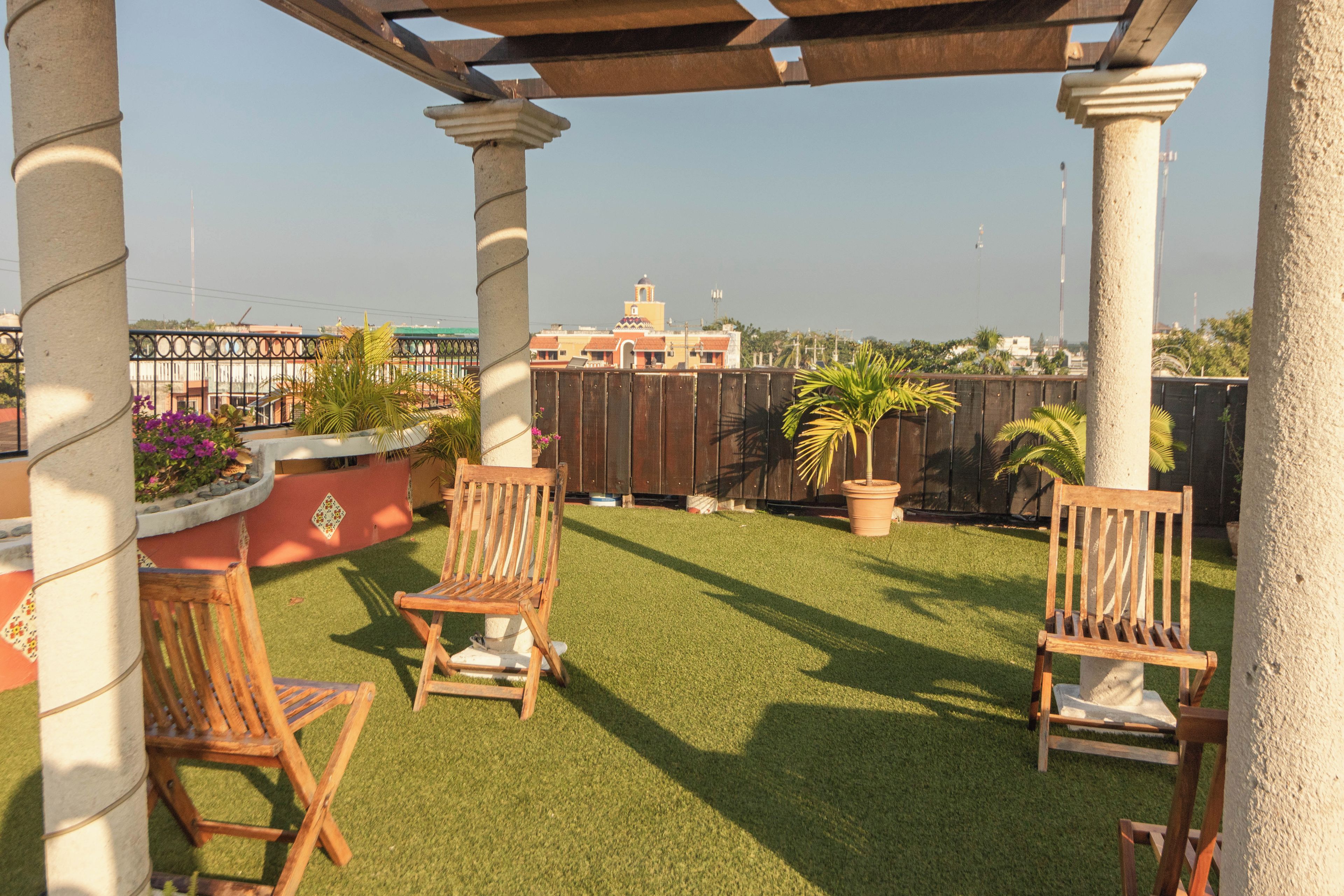 A patio with artificial grass, wooden chairs, and planters.