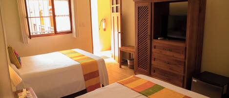 A hotel room with two beds, a television, a cabinet, and a window with curtains.
