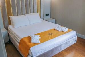 A neatly made bed with white linens, a gold accent throw, and a towel folded on the bed.
