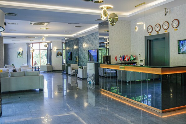 A modern hotel lobby with a reception desk, seating area, and large windows.