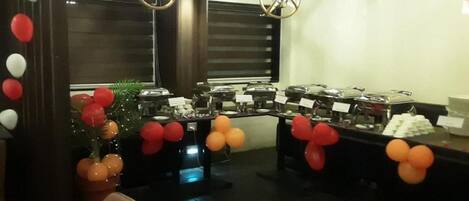 Una sala con mesas dispuestas para un bufé, decorada con globos y un árbol de Navidad adornado.