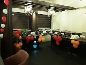 A room with tables set up for a buffet, decorated with balloons, and a Christmas tree with ornaments. - The Fern Leo Beach Resort (Porbandar)