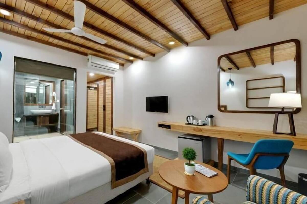 Una habitación de hotel con cama, escritorio, silla, televisor y espejo.