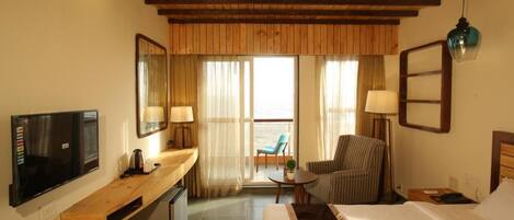 Habitación de hotel con cama, escritorio, silla, televisor y balcón con vistas.