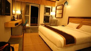 A hotel room with a bed, a desk, a chair, a small table, and a balcony with curtains.
