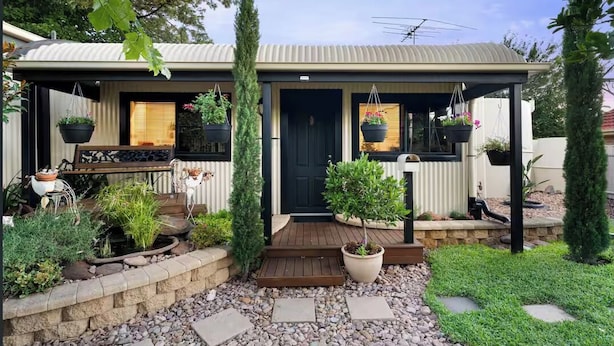 Une maison moderne dotée d’un porche abrité, de plantes en pot et d’un petit jardin.