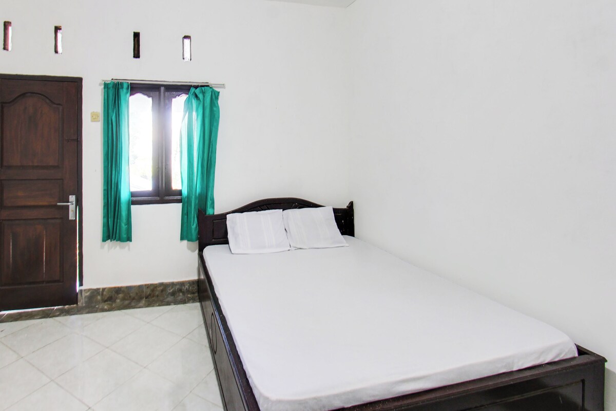 Een slaapkamer met een bed, een raam met gordijnen, een deur en een betegelde vloer.