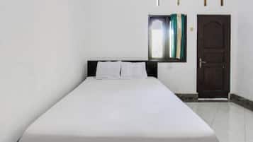 Een eenpersoonsbed met witte lakens in een kamer met witte wanden, een houten deur en een raam met gordijnen.