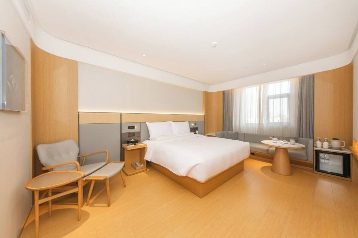 A modern hotel room with a bed, a desk, a chair, a small table, and a TV.