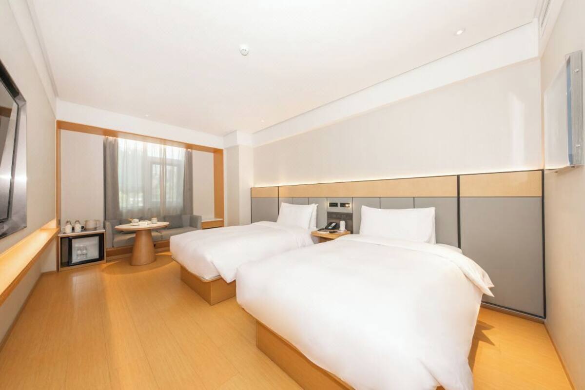 A hotel room with two beds, a small table, a TV, and a mirror.