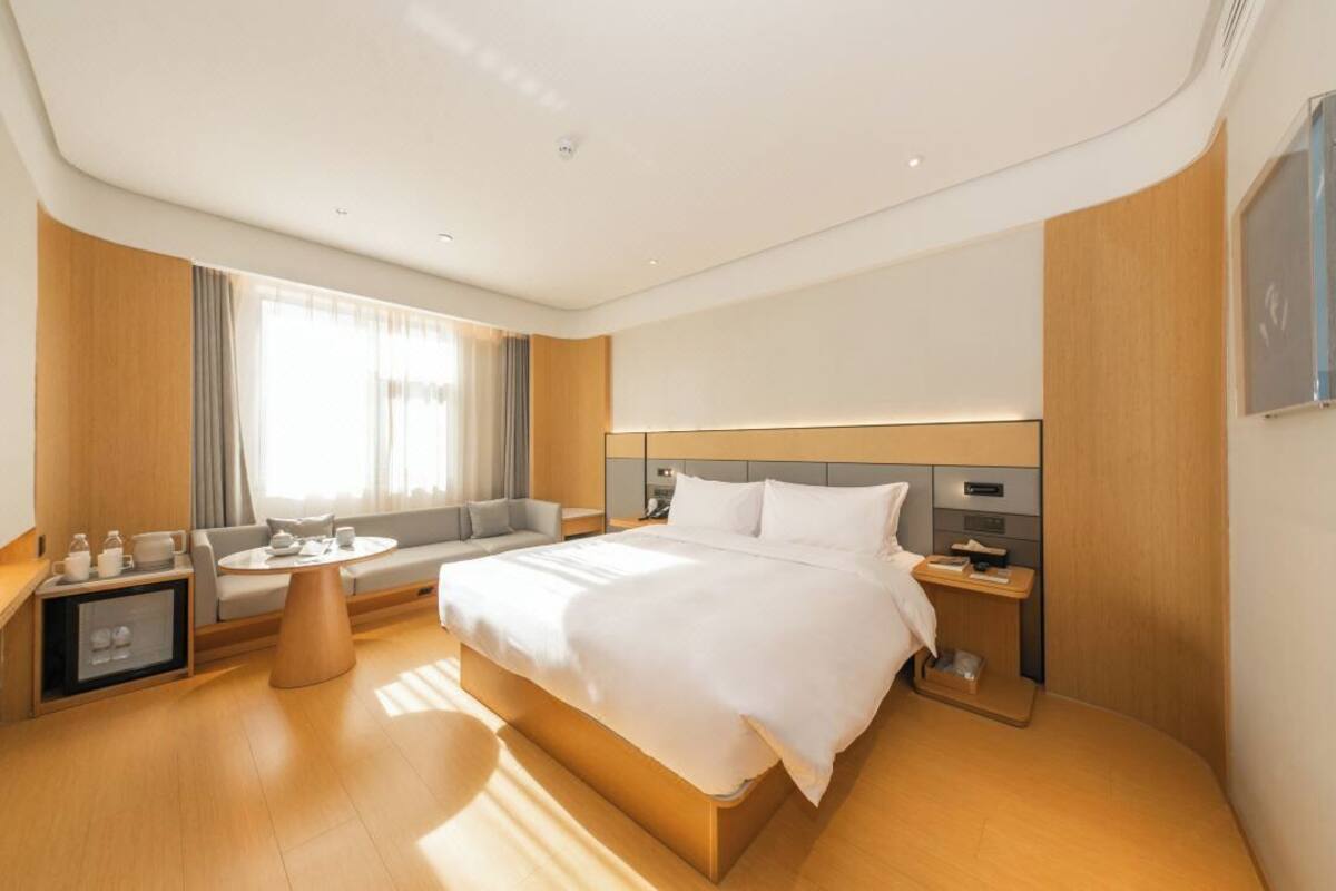 A modern hotel room with a large bed, a sofa, a small round table, and a nightstand.
