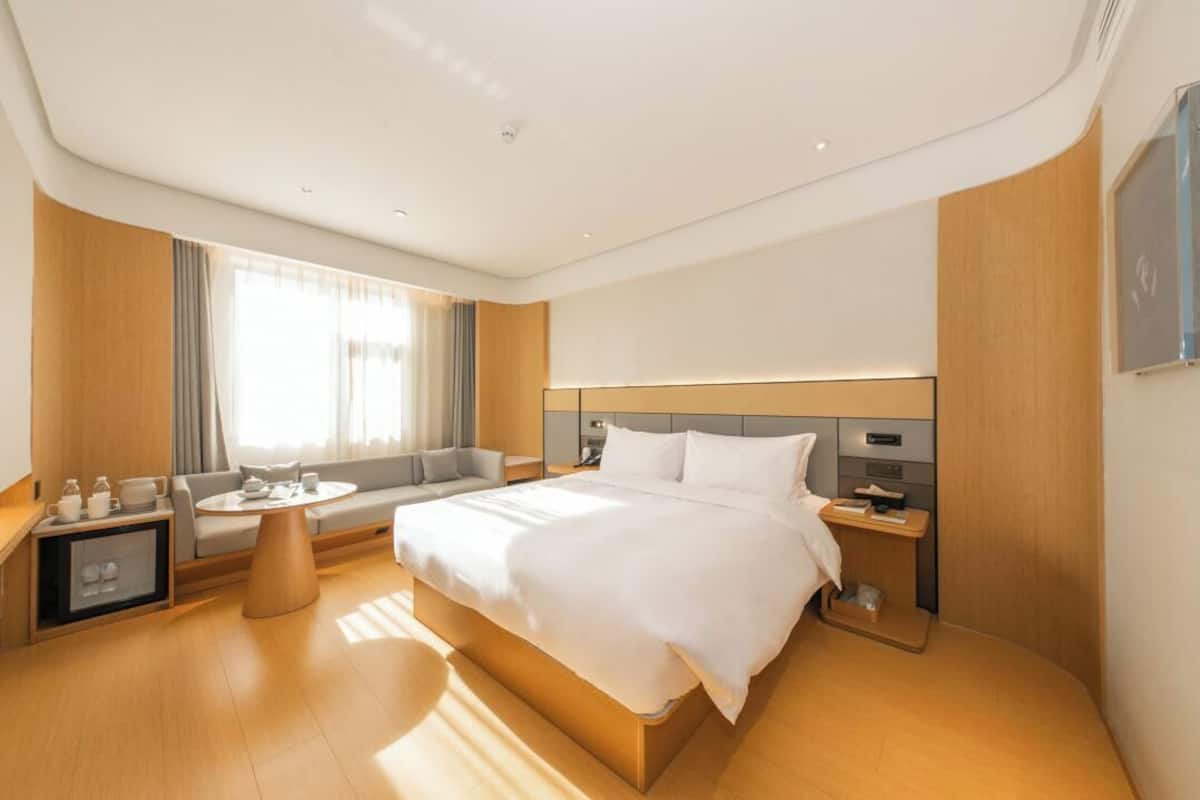 Una habitación de hotel moderna con una cama grande, un sofá, una pequeña mesa redonda y una mesita de noche.