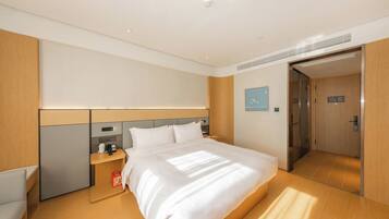 Una habitación de hotel moderna con una cama grande, una mesita de noche y un panel de control en la pared, además de una puerta que da a un baño.