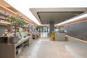 A modern hotel lobby with a reception desk, seating area, and a large plant. - Ji Hotel Gu An Daxing International Airport (Langfang)